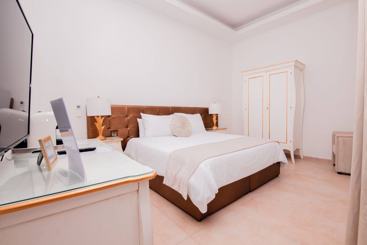 A modern bedroom with a bed, bedside tables, a desk with a laptop, and a wardrobe.