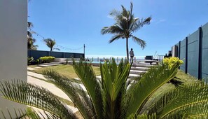 Un espace piscine offrant une vue sur l’océan, avec des palmiers et une personne debout près de la piscine.