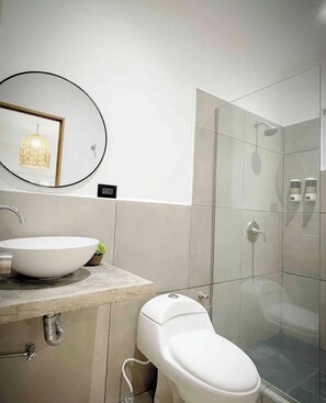 A modern bathroom with a round mirror, a white sink, a toilet, and a glass-enclosed shower.