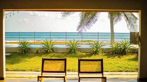 A beach view from a window with two wooden chairs facing the ocean, palm trees, and a fence. - Villa Marr, Beachfront House in La Libertad (San Salvador)