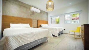 A hotel room with two beds, a wooden headboard, an air conditioning unit, a yellow chair, and a window with a view of greenery. - Villa Marr, Beachfront House in La Libertad (San Salvador)