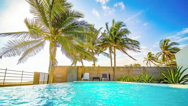 A swimming pool with palm trees, lounge chairs, and a concrete wall. - Villa Marr, Beachfront House in La Libertad (San Salvador)