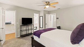 A bedroom with a bed, a ceiling fan, a TV on a stand, and a door leading to another room. - Palmetto Retreat/Centrally Located/Near FLETC (Brunswick)