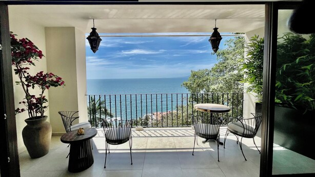 Ein Balkon mit Meerblick, der zwei Hängelampen, einen Kübel mit einer Pflanze und zwei Stühle zeigt.