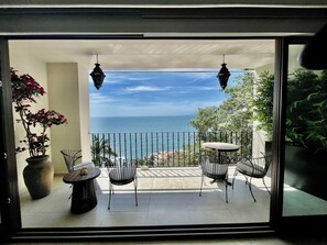 Ein Balkon mit Meerblick, der zwei Hängelampen, einen Kübel mit einer Pflanze und zwei Stühle zeigt.