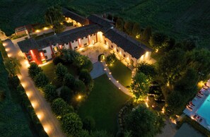 An aerial view of a well-lit, multi-story building with a courtyard, surrounded by greenery. - La Corte San Lorenzo  (Moscazzano)