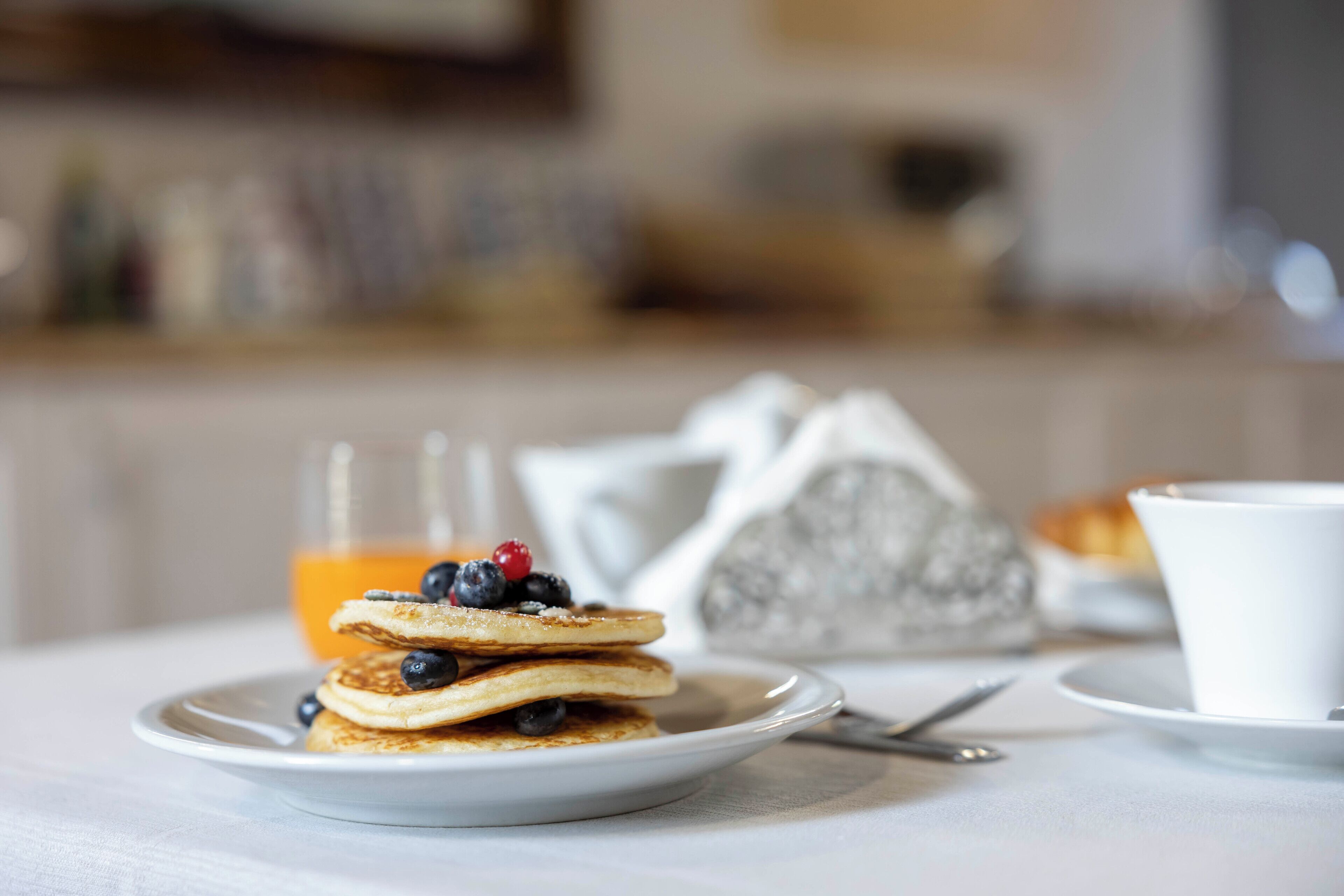 A breakfast setting with pancakes topped with blueberries and a glass of orange juice.