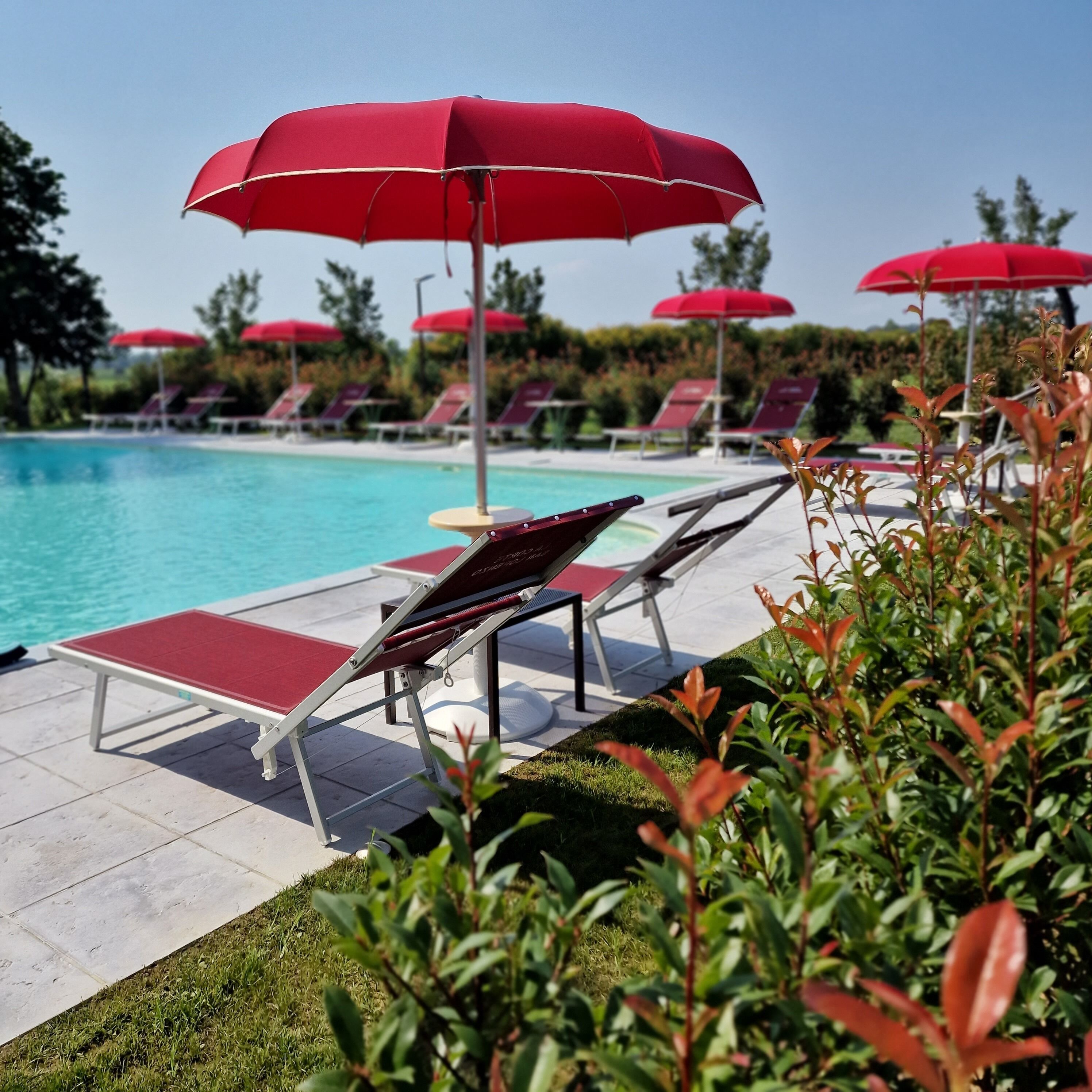Un espace aménagé au bord de la piscine, avec des parasols rouges, des chaises longues et une piscine à l’eau d’un bleu limpide.