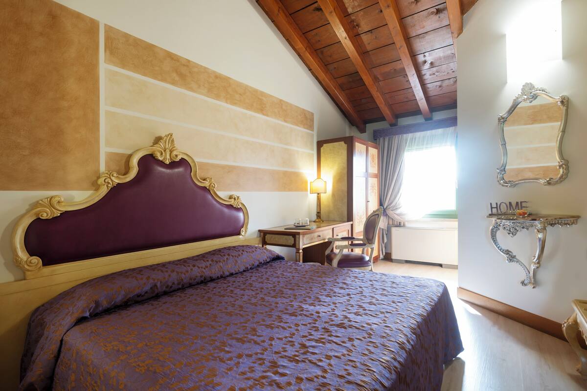 A bedroom with a large bed, a desk, and a chair. There is a mirror on the wall and a sign that says "HOME".