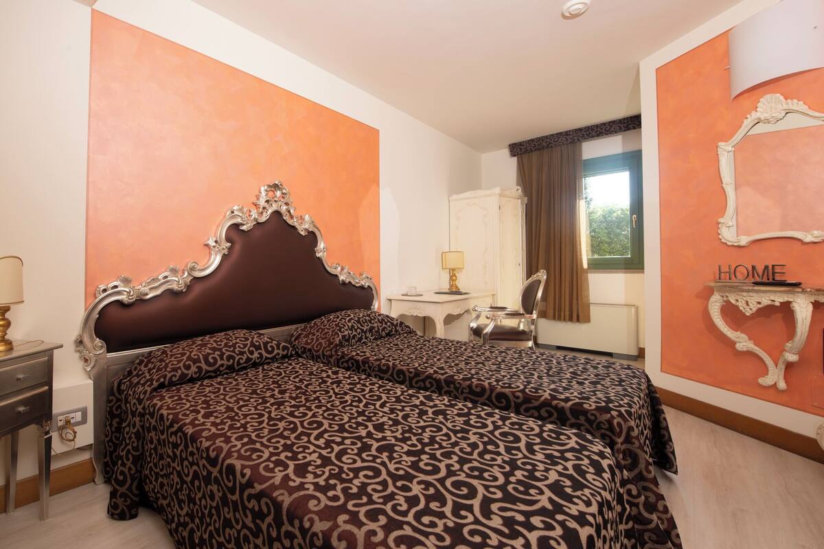 A hotel room with a large bed, a desk, a chair, and a wardrobe.