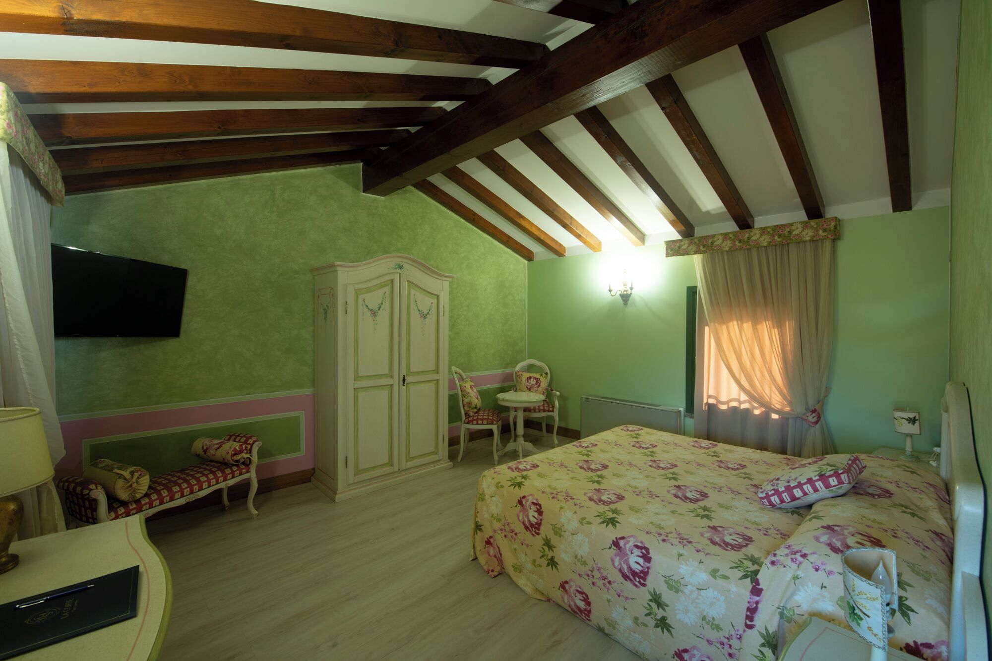 A bedroom with a bed, a wardrobe, a chair, a table, and a television.