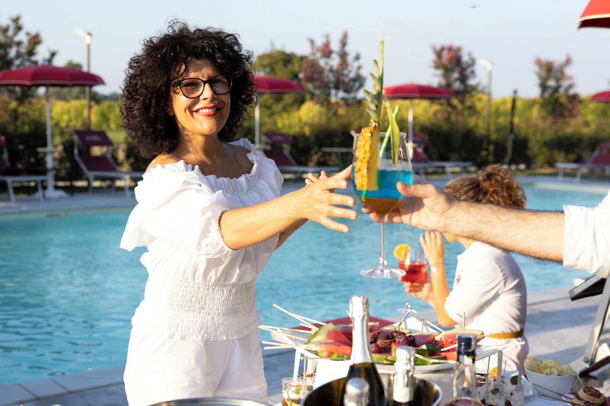 Ein Essbereich am Pool mit gedecktem Tisch, einer Champagnerflasche und einem tropischen Getränk.