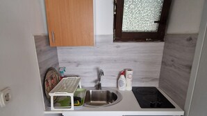 Une petite cuisine équipée comprenant un évier, un petit réfrigérateur et une fenêtre ornée d’un motif texturé.