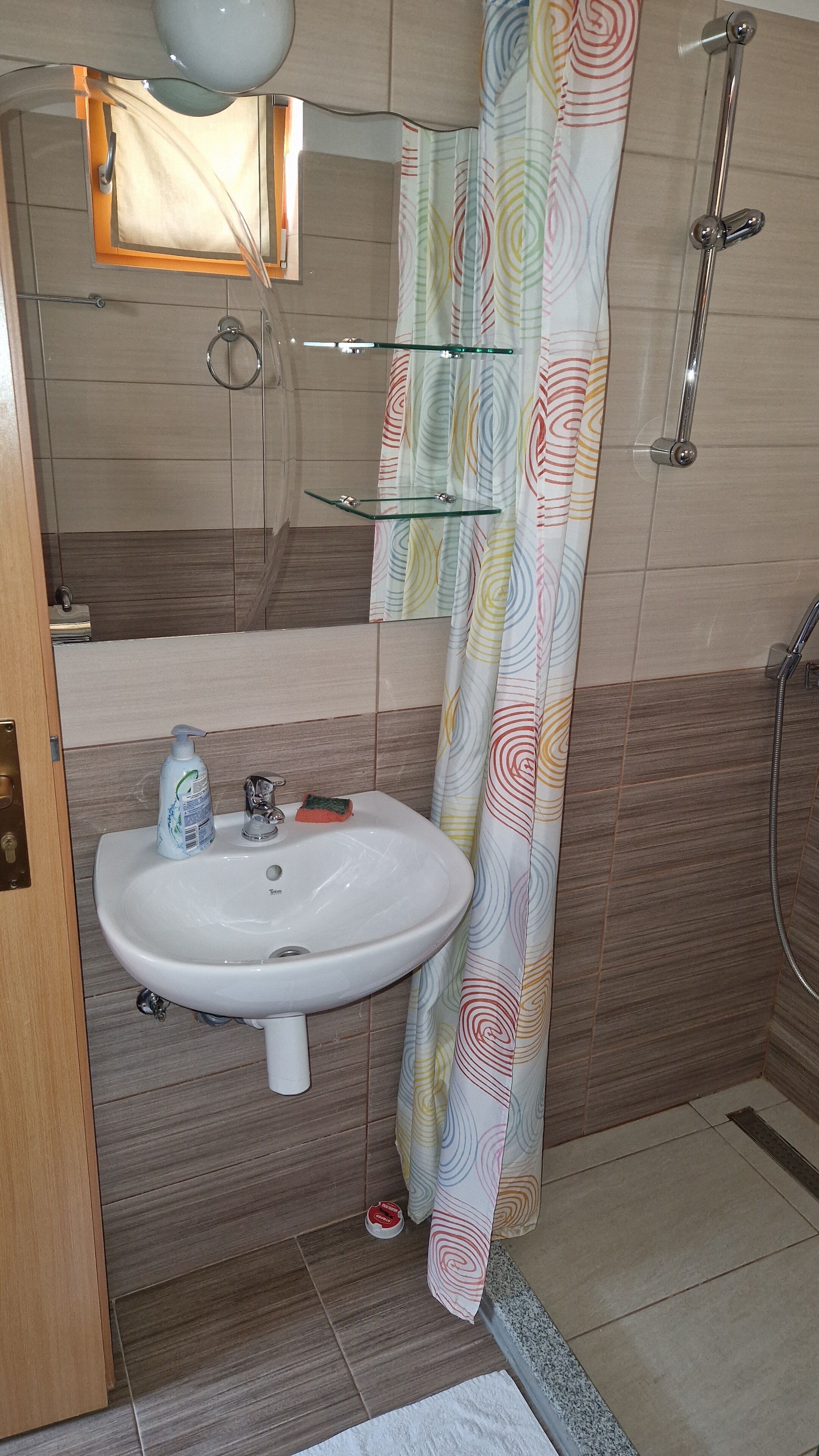 A bathroom with a white sink, a glass shelf, a shower, and a colorful shower curtain.