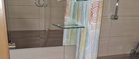 A bathroom with a white sink, a glass shelf, a shower, and a colorful shower curtain.