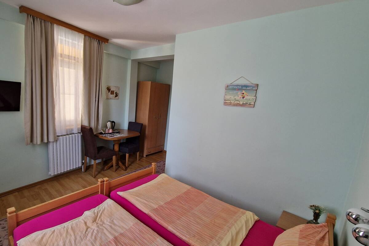 A hotel room with two beds, a desk with a chair, a television, and a wardrobe.