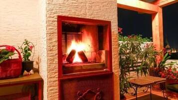 Una chimenea de piedra con fuego, rodeada de plantas en macetas y un banco de madera.