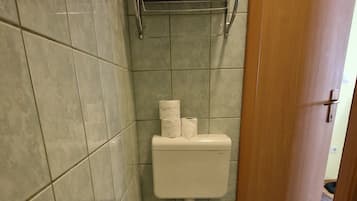 A bathroom with a toilet, a shelf with towels, and a roll of toilet paper.