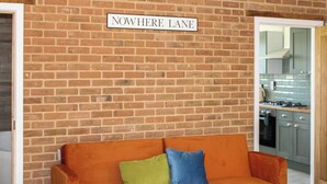 A brick wall with a sign reading 'NOWHERE LANE' and a modern kitchen visible through an open doorway.