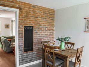 A dining area with a brick wall, a chalkboard with a welcome message, wooden chairs, a table with a green pitcher, and a bowl of food.