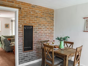 Un comedor con pared de ladrillo, un letrero de pizarra, muebles de madera y un florero verde.