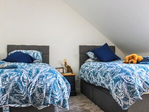 Two twin beds with matching blue leaf-patterned bedding, a nightstand with a lamp, and a teddy bear on the right bed.