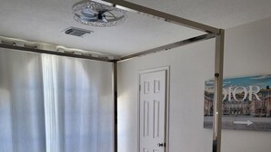 Et soveværelse med seng, ventilator, dør og et billede på væggen.