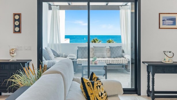A modern living room with a large sliding glass door leading to a balcony with a view of the sea. - Apartment in Playas del Duque for 5 people | Casa Cadiz 412A (Puerto Banús - Marbella)