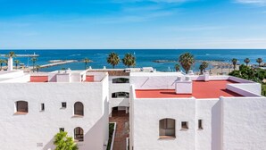 A coastal building with white walls and red roofs, overlooking a beach with palm trees and the sea. - Apartment in Playas del Duque for 5 people | Casa Cadiz 412A (Puerto Banús - Marbella)