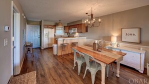 A spacious kitchen with wooden flooring, a dining area with a wooden table and chairs, and a chandelier. - New Listing-Open weeks in prime summer time! Cozy condo, ocean views & pool.   (Rodanthe)