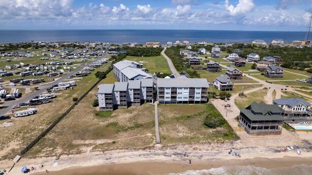 A coastal area with a large RV parking lot, beachfront properties, and a prominent building with multiple floors and balconies. - New Listing-Open weeks in prime summer time! Cozy condo, ocean views & pool.   (Rodanthe)