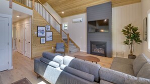 Uma sala de estar moderna com escada de madeira, sofás cinzas, lareira e televisão de tela plana.