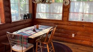 A wooden cabin interior with a dining table, chairs, a rug, and a chandelier.
