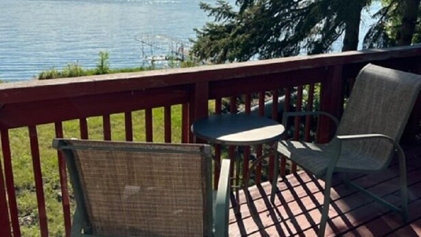 A wooden deck with a table and two chairs, overlooking a body of water and trees.
