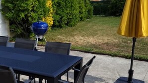 An outdoor patio with a table and chairs, a barbecue grill, and a yellow umbrella.