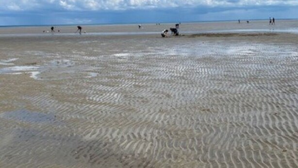 A beach with rippled sand patterns and a clear blue sky with scattered clouds.