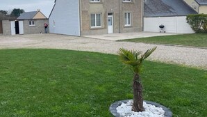 A two-story house with a sloped roof, a gravel driveway, and a small lawn with a palm tree.