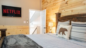 A hotel room with a wooden interior, a bed with a quilted bedspread, a pillow with a bear design, a bedside lamp, and a wall-mounted TV displaying "NETFLIX". - Lake side retreat- Huge game room, hot tub fire pit and more! (Sevierville)