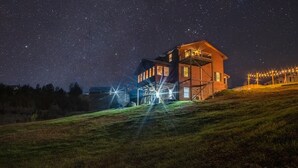 A wooden house with a balcony, surrounded by a grassy hill and a starry night sky. - Lake side retreat- Huge game room, hot tub fire pit and more! (Sevierville)