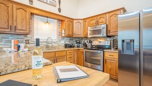 A kitchen with wooden cabinets, stainless steel appliances, a granite countertop, and a bottle of Winking Oil. - Lake side retreat- Huge game room, hot tub fire pit and more! (Sevierville)