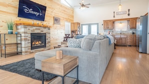 A spacious living room with a fireplace, a grey sofa, and a flat-screen TV mounted on the wall. - Lake side retreat- Huge game room, hot tub fire pit and more! (Sevierville)