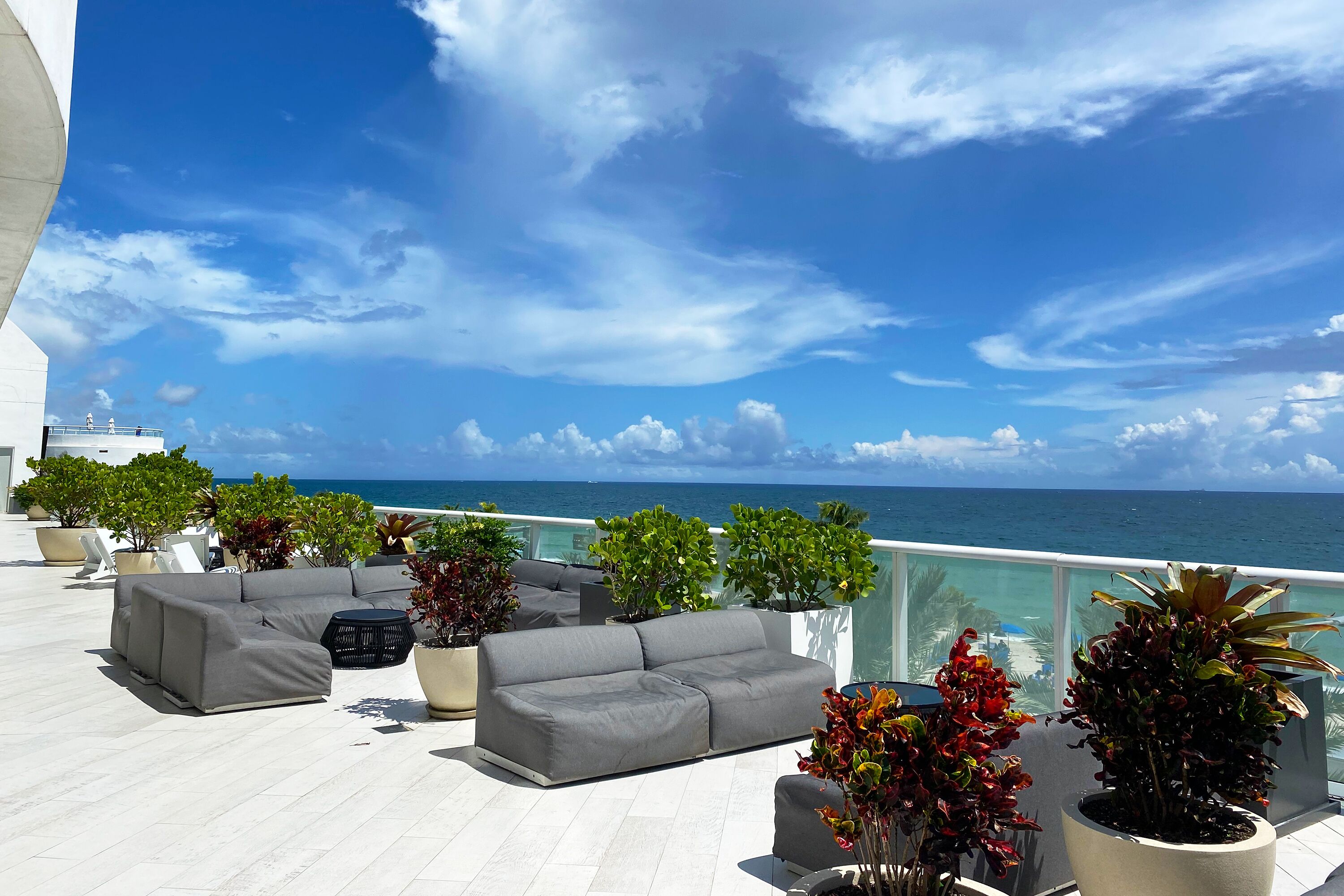 A rooftop terrace with a grey sofa set, potted plants, and a view of the ocean.