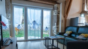 A cozy living room with a leather sofa, a wooden coffee table, and a large sliding glass door leading to a garden. - Gîte La Bergerie 5/6 Pers (LACHAMP-RIBENNES)