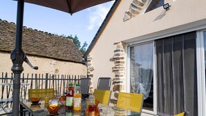 An outdoor patio with a glass table and yellow chairs, a grill, and a stone wall. - Gîte La Bergerie 5/6 Pers (LACHAMP-RIBENNES)