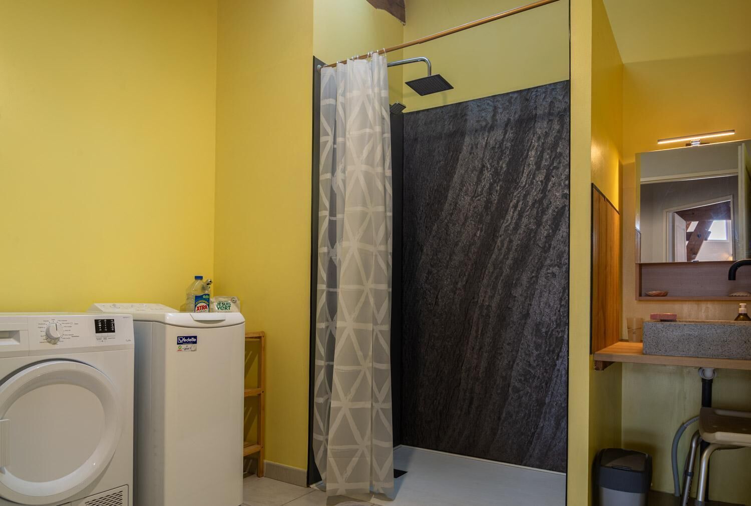 A bathroom with a washing machine, a shower with a dark marble wall, and a sink with a mirror above it.