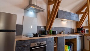 A modern kitchen with stainless steel appliances, wooden beams, and a built-in oven. - Gîte La Bergerie 5/6 Pers (LACHAMP-RIBENNES)