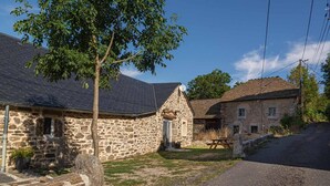 A stone building with a sloped roof, a small porch, and a picnic table. - Gîte La Bergerie 5/6 Pers (LACHAMP-RIBENNES)