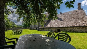 An outdoor dining area with a round table and chairs, surrounded by a stone building with a tiled roof.