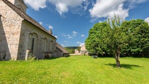 A stone building with a sloped roof, a grassy courtyard, and a large tree.