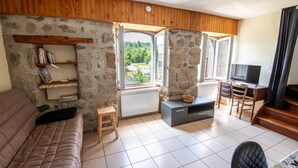A cozy living room with a stone wall, a sofa, a TV, and a view of greenery outside.